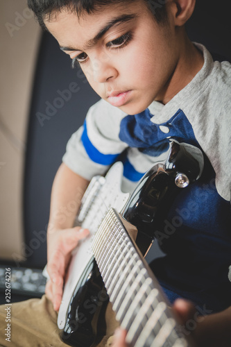 8 year old British Indian boy practices the electric guitar at home. 