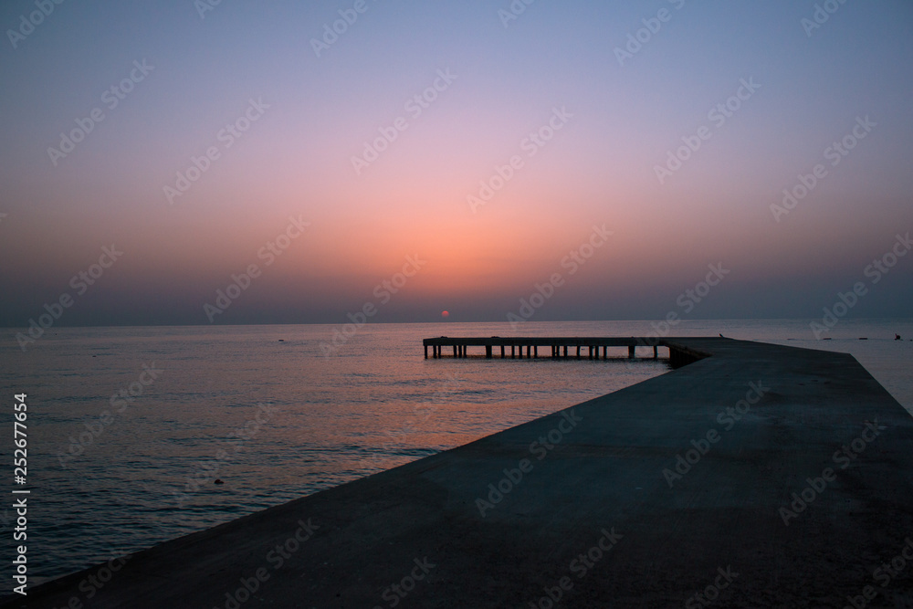 Background with old wooden pier in the sea at sunset. The sun goes down in the water.