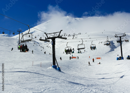 skiers, snowboarders and tourist traveling in cable cars in a snow covered misty mountain with a clear blue sky. 
