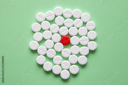 Top view of a pile of white medicine pills on a white surface. One tablet of red medication. Vaccine concept  photo