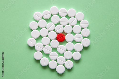 Top view of a pile of white medicine pills on a white surface. One tablet of red medication. Vaccine concept 