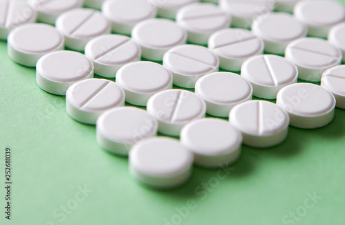 Top view of a pile of white medicine pills on a white surface. One tablet of red medication. Vaccine concept 