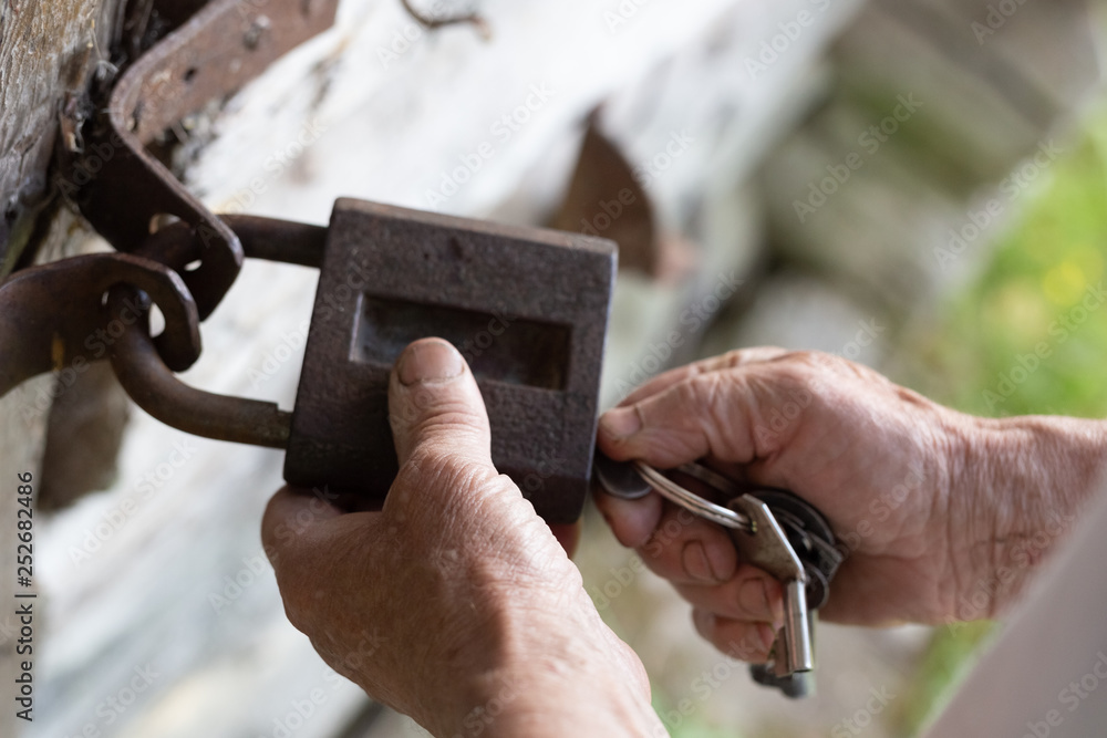 Fototapeta premium Old man hands holding metal vintage lock and key to open close old wooden door