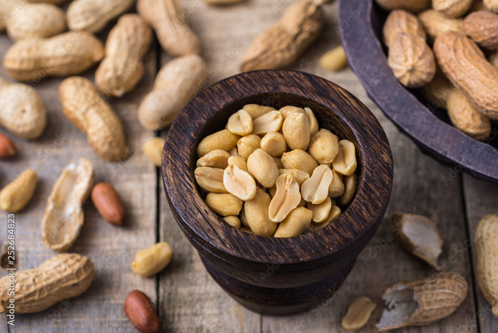Peanuts in small dark wooden bowl on natural rustic desk. Peanuts in small dark wooden bowl on natural rustic desk.