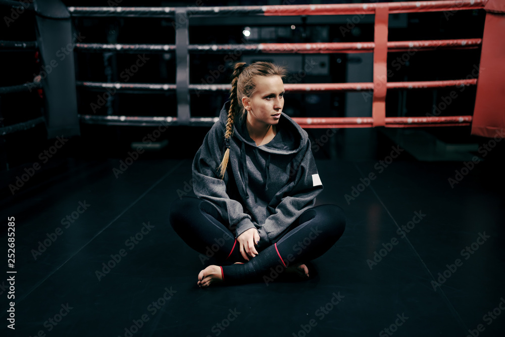 Φωτογραφία Caucasian strong boxer girl sitting in ring in sweatshirt and with bandage on feet and looking away
