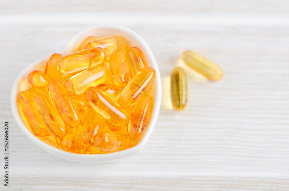 Fish oil capsules on a white wooden background, vitamin D supplement, selective focus. Fish oil capsules on a white wooden background, vitamin D supplement, selective focus.