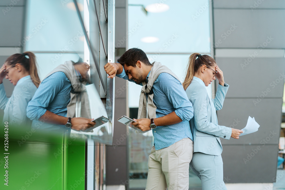 Fototapeta premium Desperate two businesspersons failing at work. They standing outdoors in front of business center and holding paperwork and tablet.