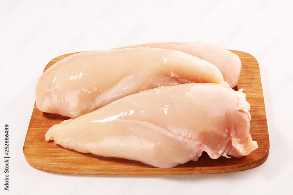 Raw chicken breasts and spices on wooden cutting board, close up Raw chicken breasts and spices on wooden cutting board, close up