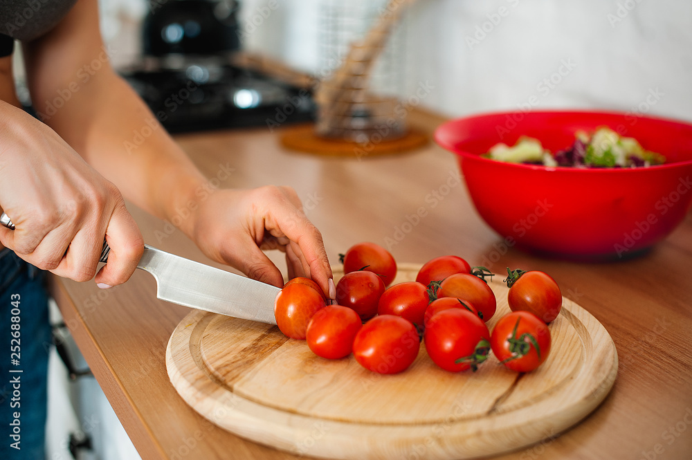 close up of female hand cutting tomato on cutting board with sharp knife