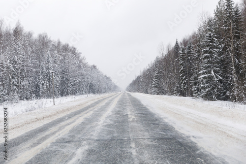 winter road with ice on the asphalt, trees under snow during the winter frost in Russia