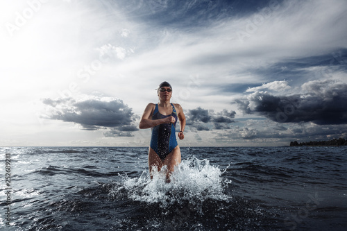 Fotografie Young woman in swimsuit running in the water during triathlon competition