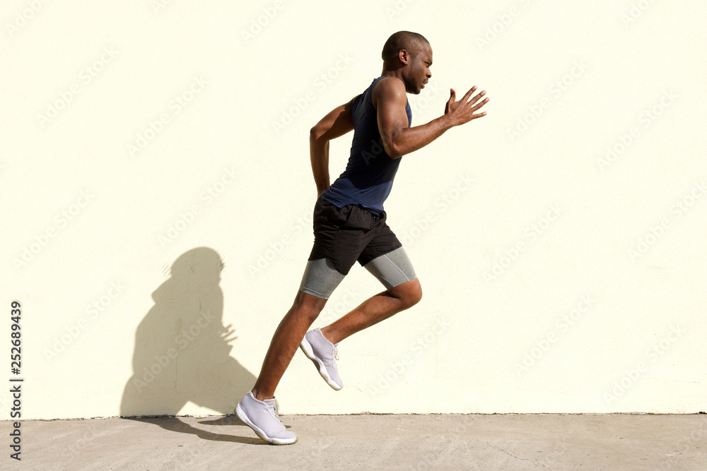 Full body profile of healthy young black man running by wall Full body profile of healthy young black man running by wall
