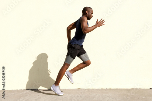 Full body profile of healthy young black man running by wall