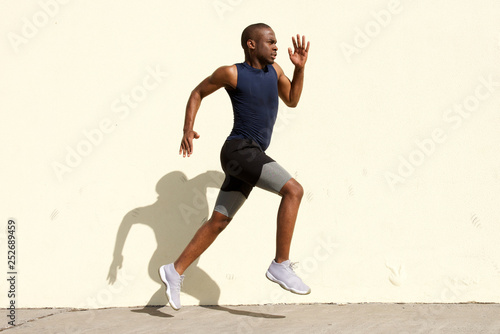 Full body side of healthy young black man running by wall