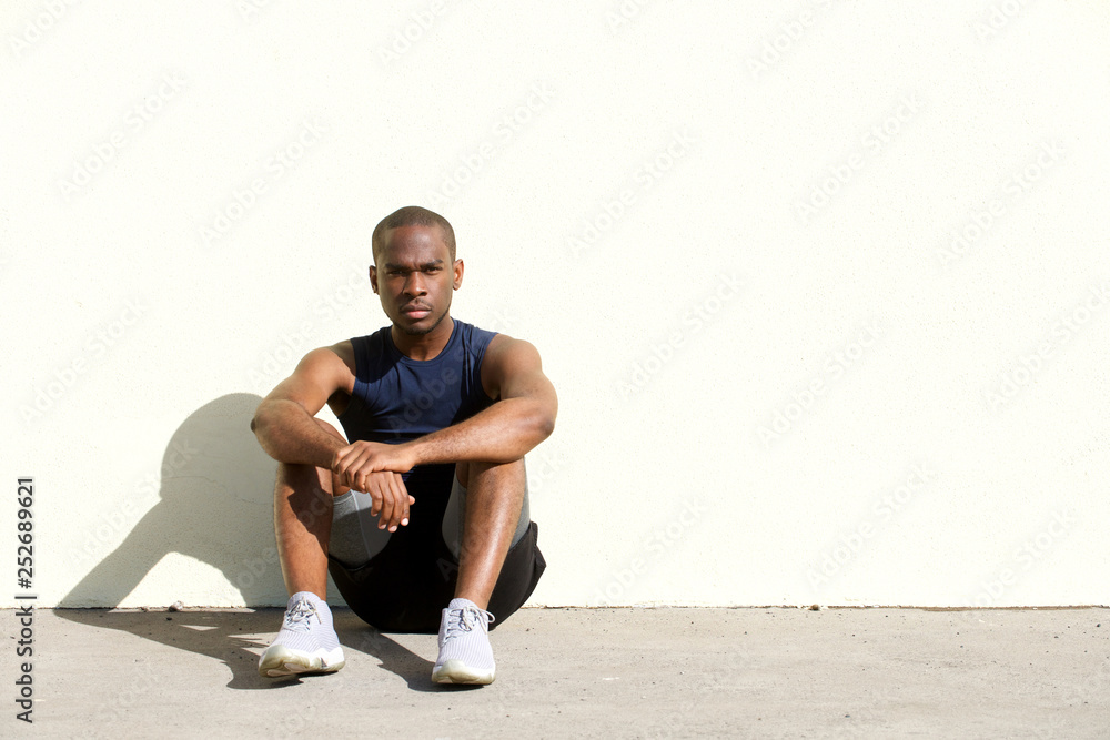 sporty young african american man sitting on floor by wall sporty young african american man sitting on floor by wall