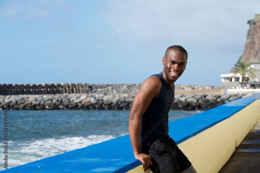 sporty african american  man leaning against wall by sea