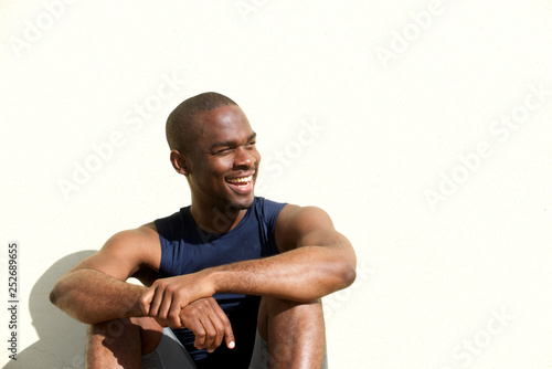Close up handsome young black man sitting by wall outdoors
