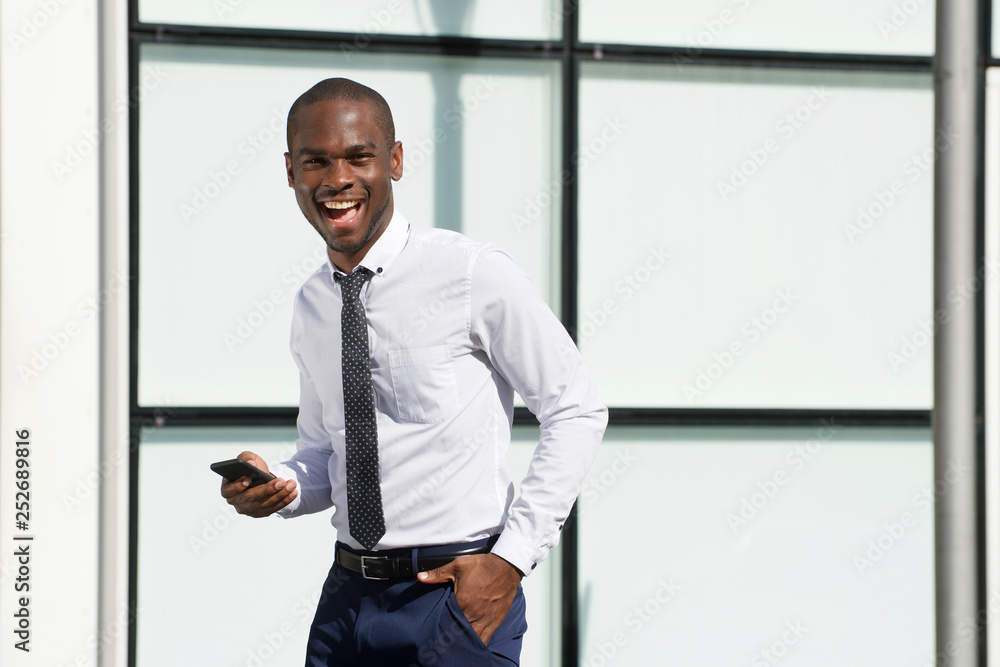 Fototapeta premium handsome african american businessman walking with mobile phone in city
