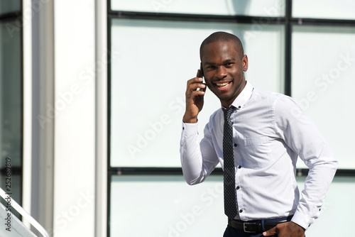 happy african american businessman walking and talking with cellphone