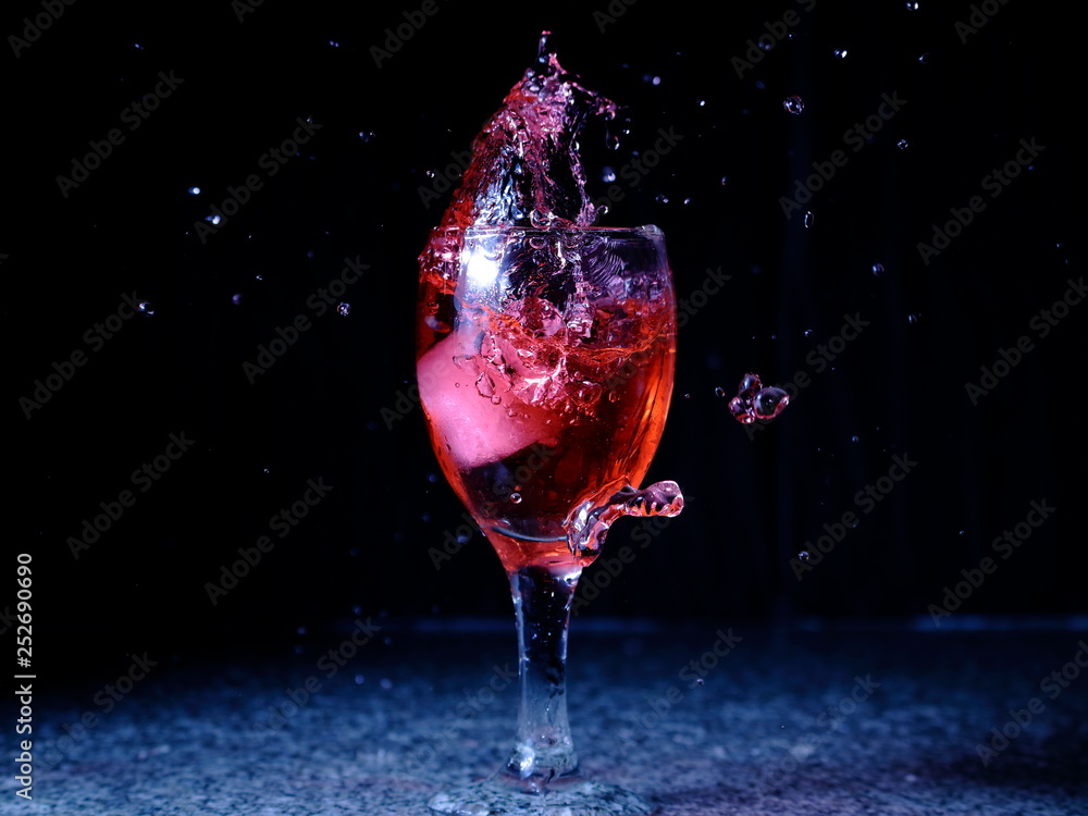 Frozen moving image. Ice falling on a glass with drink that spills and splashes.