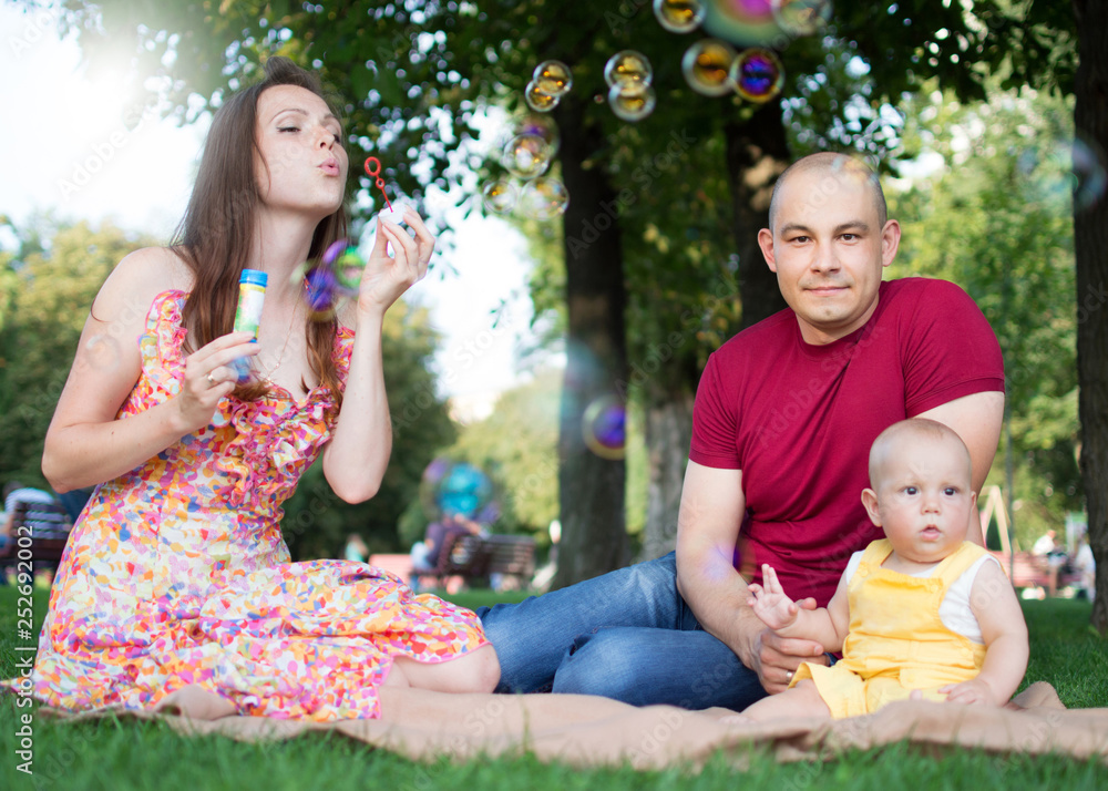 Family weekend. Mother father and son in a summer park are sitting on a green lawn Family weekend. Mother father and son in a summer park are sitting on a green lawn