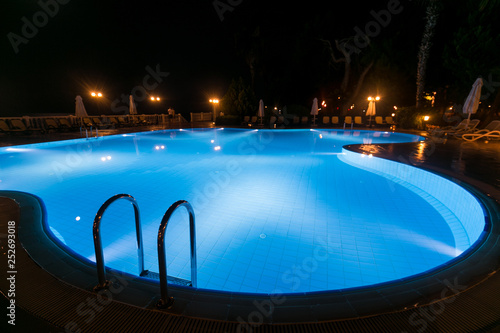 Illuminated swimming pool at night time. Grab bars ladder in the blue swimming pool at tropical resort. © stone36