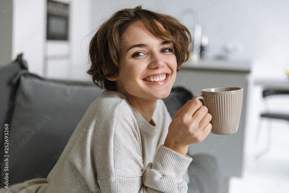 Happy young woman sitting on a couch at home Happy young woman sitting on a couch at home
