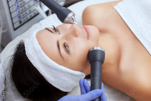 The cosmetologist makes the procedure an ultrasonic cleaning of the facial skin of a beautiful, young woman in a beauty salon.Cosmetology and professional skin care. photo