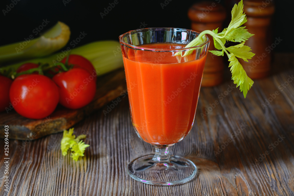 Fresh tomato juice in a glass goblet with a celery sprig and a tomato twig in the background in a low key Fresh tomato juice in a glass goblet with a celery sprig and a tomato twig in the background in a low key