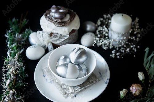 Traditional Easter cake with silver painted eggs, candles and willow on a black background. Selective focus