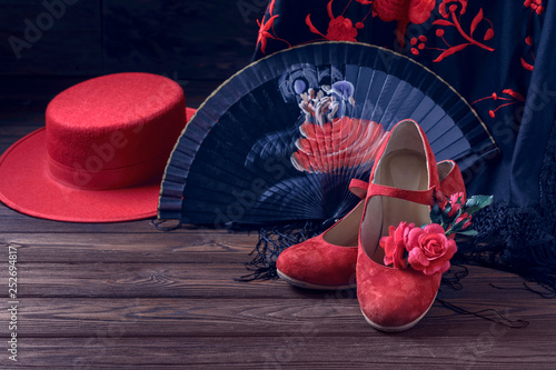 Beautiful and bright accessories for flamenco dance on a wooden background in a low key with free space. Shawl, hat, fan, shoes and a flower for the hair.