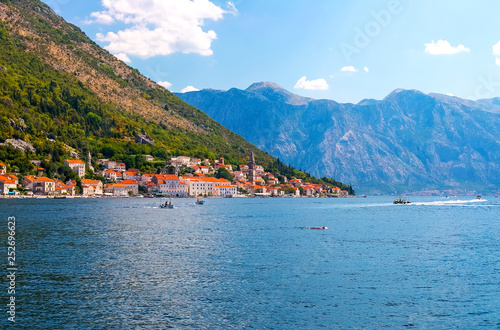 Incredible bright seascape. View of green wooded mountains and blue sea, blue sky and white clouds and a yacht sailing through the waves between the mountains. Boka Kotorska Bay, Montenegro © Natallia