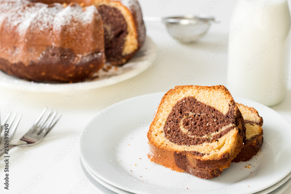 Marble bundt cake slaces on a white festive table set with milk and plates. Whole grain healthy rustic bakery. Marble bundt cake slaces on a white festive table set with milk and plates. Whole grain healthy rustic bakery.