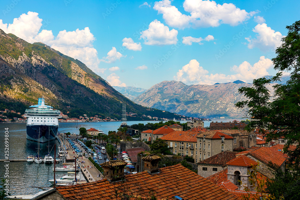 Scenic panoramic view of the historical city of Kotor on the shore of which there is an airliner located in the Bay of Kotor among mountains, on a sunny day, Montenegro
