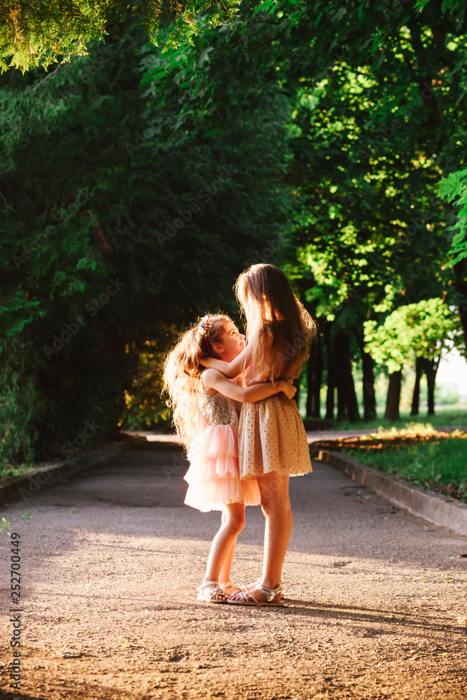 Two Cute little girls hugging and laughing at the garden at warm summer evening. Happy kids outdoors concept. Soft focused Two Cute little girls hugging and laughing at the garden at warm summer evening. Happy kids outdoors concept. Soft focused