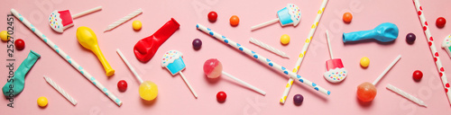 Flat lay childs birthday party, pink background (pattern). Sweet candies, bright balloon, festive candles, cupcake and straws.