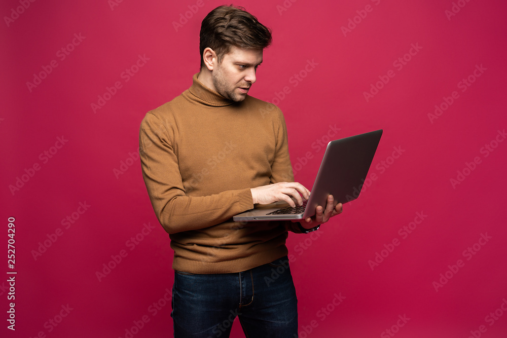 Picture of handsome man in casual holding laptop and chatting or working isolated over pink background. Picture of handsome man in casual holding laptop and chatting or working isolated over pink background.
