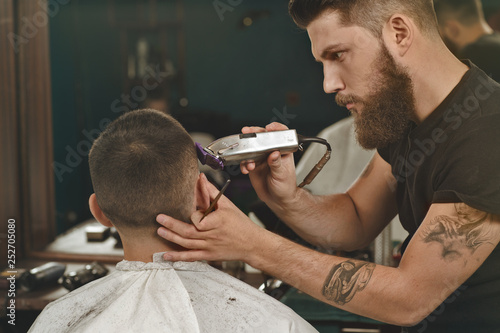 Some styling here. Horizontal shot of a handsome bearded and tattooed giving a haircut to the young man trimming his hair