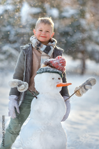 Smiling boy making cute snowman in the forest. Winter vacation
