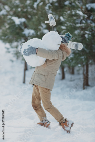 The boy is building a snowman. Boys building a snow man playing outside on a sunny snowy winter day. Outdoor family holiday on the Christmas holidays. Boy and girl playing snowballs.