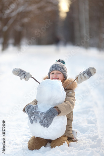 The boy is building a snowman. Boys building a snow man playing outside on a sunny snowy winter day. Outdoor family holiday on the Christmas holidays. Boy and girl playing snowballs.