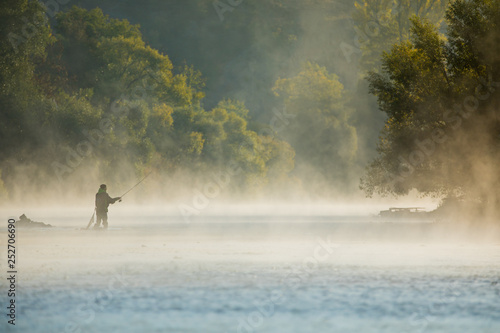 Fototapeta Men fishing in river with fly rod during summer morning