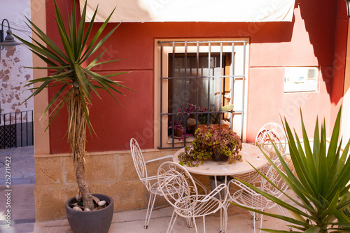 Small patio with white metal-woven tables and chairs and flower pots in the old city of Finestrat Spain © Ирина Селина