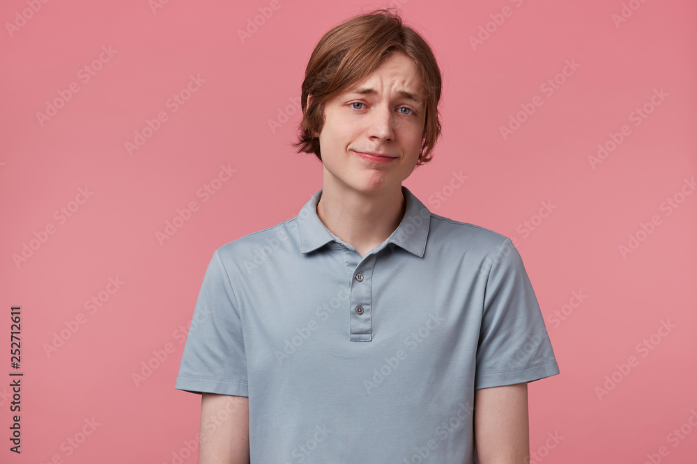 Cheerful pleased european guy with blue eyes neatly combed looks carefree optimistic dressed in elegant T-shirt in good mood while posing in studio against pink background. Facial expressions concept Cheerful pleased european guy with blue eyes neatly combed looks carefree optimistic dressed in elegant T-shirt in good mood while posing in studio against pink background. Facial expressions concept