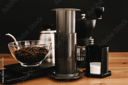 Aeropress  steel kettle  scales  manual grinder  coffee beans on wooden table and black background. Alternative coffee brewing method set. Stylish accessories and items for alternative coffee