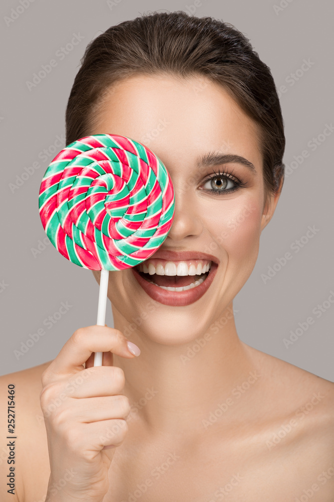 Cheerful smiling woman with big colorful lollipop. Gray background.