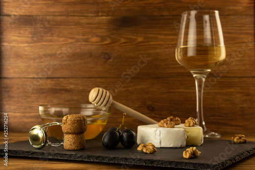 Chopped camembert cheese  nuts  honey  sweet grapes and cork from wine bottle on the background of a glass of white dry wine