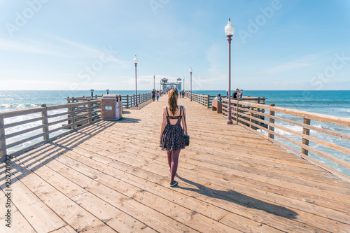 Mulher caminhando sobre píer de madeira, em um dia de sol, usando vestido, em Oceanside, cidade da California dos EUA