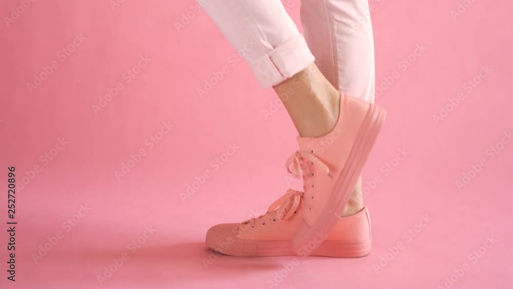 Close up of shapely young female legs walking in fashionable sneakers on coral background Close up of shapely young female legs walking in fashionable sneakers on coral background
