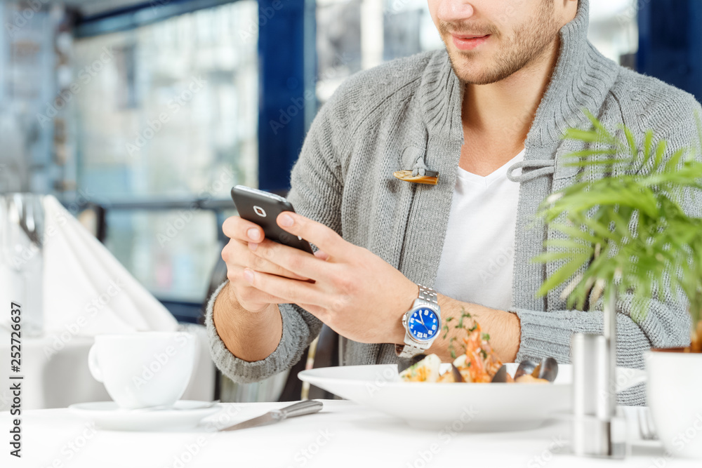 Have to answer this. Cropped shot of a young casual man texting on his phone over lunch in a restaurant Have to answer this. Cropped shot of a young casual man texting on his phone over lunch in a restaurant